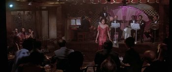 Movie still from “Lady Sings the Blues” (1972), directed by Sidney J. Furie – A group of people sitting in a room with a woman in a red dress; Wide shot, High angle