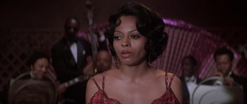 Movie still from “Lady Sings the Blues” (1972), directed by Sidney J. Furie – A woman in a red dress is in front of a group of people; Close Up shot, Over the shoulder angle