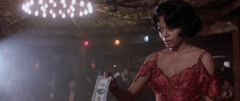 Movie still from “Lady Sings the Blues” (1972), directed by Sidney J. Furie – A woman in a red dress holding a $ 1 0 0 bill; Close Up shot, Low angle