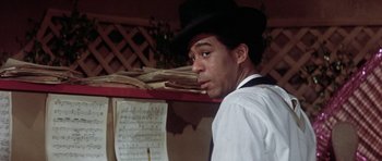 Movie still from “Lady Sings the Blues” (1972), directed by Sidney J. Furie – A man wearing a black hat standing in front of a sheet of music; Close Up shot, Over the shoulder angle