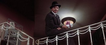 Movie still from “Lady Sings the Blues” (1972), directed by Sidney J. Furie – A man sitting on top of a railing holding a present; Medium shot, Low angle