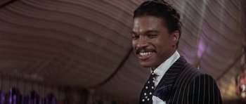 Movie still from “Lady Sings the Blues” (1972), directed by Sidney J. Furie – A man wearing a suit and tie smiling for the camera; Close Up shot, Low angle