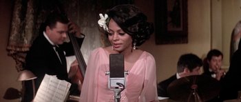 Movie still from “Lady Sings the Blues” (1972), directed by Sidney J. Furie – A woman in a pink dress standing in front of a microphone; Close Up shot, High angle