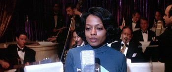 Movie still from “Lady Sings the Blues” (1972), directed by Sidney J. Furie – An african american woman in a blue top is holding a microphone; Close Up shot, Over the shoulder angle
