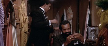 Movie still from “Lady Sings the Blues” (1972), directed by Sidney J. Furie – A man sitting in front of another man holding a pair of scissors; Medium shot, Over the shoulder angle