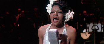 Movie still from “Lady Sings the Blues” (1972), directed by Sidney J. Furie – A woman singing into a microphone in front of a crowd of onlookers; Close Up shot, High angle