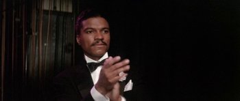Movie still from “Lady Sings the Blues” (1972), directed by Sidney J. Furie – A man in a tuxedo clapping his hands in front of a black background; Close Up shot, Low angle