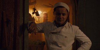 A man in a chef's outfit leaning against a wall