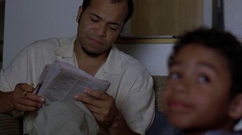 Movie still from “Lady in the Water” (2006), directed by M. Night Shyamalan – A man sitting on a couch looking at a newspaper; Close Up shot, Low angle