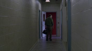 Movie still from “Lady in the Water” (2006), directed by M. Night Shyamalan – A man standing in a hallway holding a bag; Wide shot, Low angle