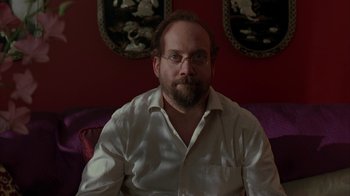 Movie still from “Lady in the Water” (2006), directed by M. Night Shyamalan – A man sitting on a couch wearing a white shirt; Medium shot, Low angle