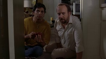 Movie still from “Lady in the Water” (2006), directed by M. Night Shyamalan – Two men sitting on the ground looking at a phone; Medium shot, High angle