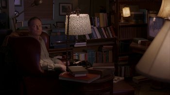 Movie still from “Lady in the Water” (2006), directed by M. Night Shyamalan – A person sitting in a chair with a lamp; Wide shot, High angle
