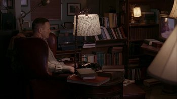 Movie still from “Lady in the Water” (2006), directed by M. Night Shyamalan – A man sitting at a table with a lamp on top of it; Wide shot, High angle