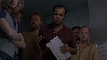 Movie still from “Lady in the Water” (2006), directed by M. Night Shyamalan – A group of men standing in a dark room holding papers; Medium shot, Low angle