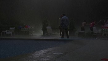 Movie still from “Lady in the Water” (2006), directed by M. Night Shyamalan – A man and a woman standing next to a pool in the rain; Extreme Wide shot, High angle