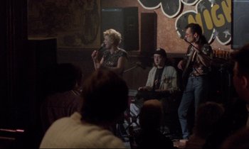 Movie still from “Ladybird Ladybird” (1994), directed by Ken Loach – A group of people in a room with a microphone; Wide shot, Over the shoulder angle