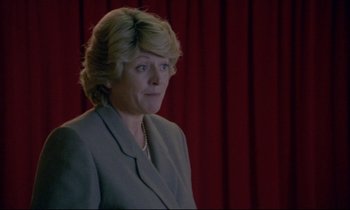 Movie still from “Ladybird Ladybird” (1994), directed by Ken Loach – A woman in a gray suit standing in front of a red curtain; Close Up shot, Over the shoulder angle