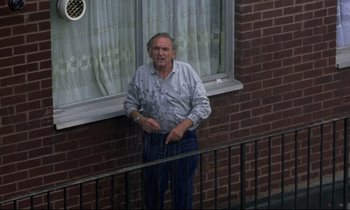 Movie still from “Ladybird Ladybird” (1994), directed by Ken Loach – An older man leaning on a railing near a window; Wide shot, High angle