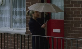 Movie still from “Ladybird Ladybird” (1994), directed by Ken Loach – A woman holding an umbrella while standing next to a building; Medium shot, Low angle