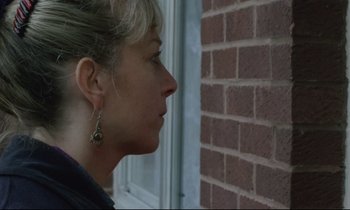 Movie still from “Ladybird Ladybird” (1994), directed by Ken Loach – A person wearing earrings near a brick wall; Close Up shot, Over the shoulder angle