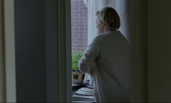 Movie still from “Ladybird Ladybird” (1994), directed by Ken Loach – A woman standing in front of a window looking outside; Medium shot, Over the shoulder angle