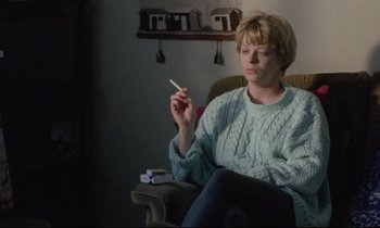 Movie still from “Ladybird Ladybird” (1994), directed by Ken Loach – A woman sitting in a chair holding a cigarette in her hand; Medium shot, High angle
