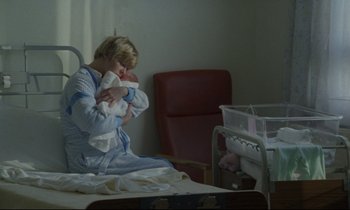 Movie still from “Ladybird Ladybird” (1994), directed by Ken Loach – A woman sitting on a hospital bed holding a baby; Medium shot, Over the shoulder angle