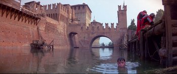 Movie still from “Ladyhawke” (1985), directed by Richard Donner – A boy swimming in a body of water near a castle; Extreme Wide shot, High angle