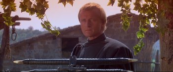 Movie still from “Ladyhawke” (1985), directed by Richard Donner – A man in a black shirt is standing in front of a building; Close Up shot, Low angle
