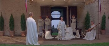 Movie still from “Ladyhawke” (1985), directed by Richard Donner – A group of people dressed in medieval garb in a room; Wide shot, Over the shoulder angle