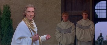 Movie still from “Ladyhawke” (1985), directed by Richard Donner – Two men dressed in medieval garb standing next to each other in front of a door; Medium shot, Low angle