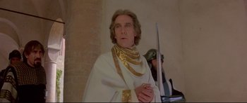 Movie still from “Ladyhawke” (1985), directed by Richard Donner – A man dressed in white and gold holding a sword; Medium shot, Low angle