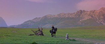Movie still from “Ladyhawke” (1985), directed by Richard Donner – A man riding a horse in a field with mountains in the background; Extreme Wide shot, Low angle
