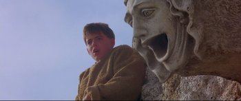 Movie still from “Ladyhawke” (1985), directed by Richard Donner – A young man standing in front of a statue of a gargoyle; Close Up shot, Low angle