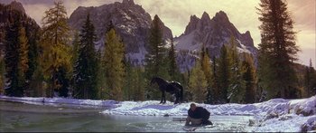 Movie still from “Ladyhawke” (1985), directed by Richard Donner – A man sitting on the ground next to a body of water with a horse in the background; Wide shot, High angle