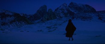 Movie still from “Ladyhawke” (1985), directed by Richard Donner – A person walking in the snow near a mountain range; Extreme Wide shot, Low angle