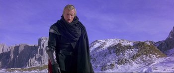 Movie still from “Ladyhawke” (1985), directed by Richard Donner – A man wearing a black cape and holding a sword in front of a snowy mountain; Medium shot, Low angle