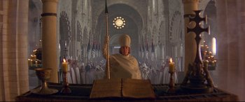 Movie still from “Ladyhawke” (1985), directed by Richard Donner – A man in a white robe holding a spear in front of a crowd of people; Wide shot, High angle