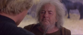Movie still from “Ladyhawke” (1985), directed by Richard Donner – An older man with a white beard is holding a pair of scissors in his hand; Close Up shot, Over the shoulder angle