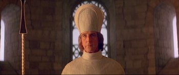 Movie still from “Ladyhawke” (1985), directed by Richard Donner – A man wearing a white hat in front of a stained glass window; Close Up shot, Low angle