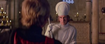 Movie still from “Ladyhawke” (1985), directed by Richard Donner – A man dressed as a priest holding a cane; Medium shot, Over the shoulder angle