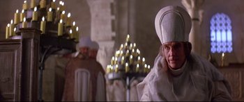 Movie still from “Ladyhawke” (1985), directed by Richard Donner – A man wearing a white hat and a white robe in front of a group of candles; Medium shot, Low angle