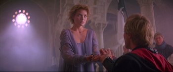 Movie still from “Ladyhawke” (1985), directed by Richard Donner – A woman in a purple dress clapping her hands; Medium shot, Over the shoulder angle