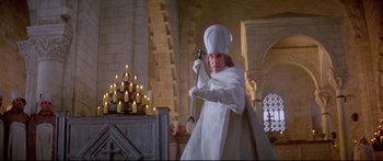 Movie still from “Ladyhawke” (1985), directed by Richard Donner – A man dressed as a priest holding a sword in front of candles; Medium shot, Low angle