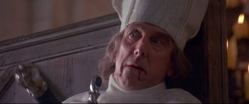 Movie still from “Ladyhawke” (1985), directed by Richard Donner – An old man wearing a chef's hat with a knife in his mouth; Close Up shot, Low angle