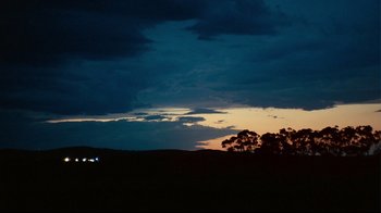 Movie still from “Lake Mungo” (2008), directed by Joel Anderson – A dark sky with some trees and a building in the background; Extreme Wide shot, Low angle
