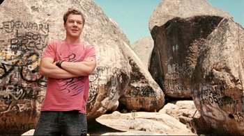 Movie still from “Lake Mungo” (2008), directed by Joel Anderson – A young man standing in front of a large rock formation; Medium shot, Low angle