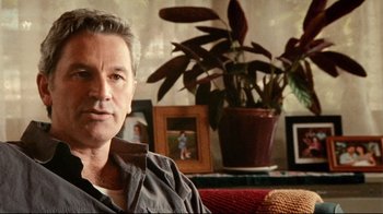 Movie still from “Lake Mungo” (2008), directed by Joel Anderson – A person sitting on a couch near a potted plant; Close Up shot, Over the shoulder angle