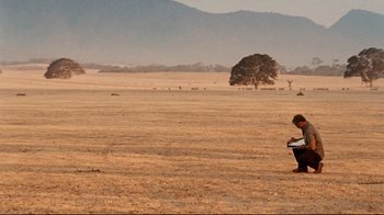 Movie still from “Lake Mungo” (2008), directed by Joel Anderson – A person standing in the middle of an empty field; Extreme Wide shot, High angle